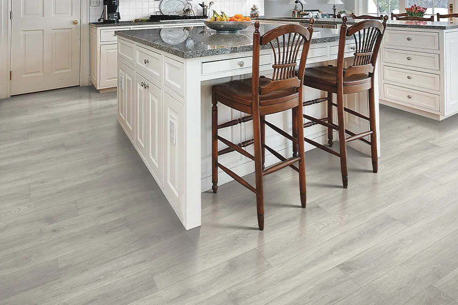 Grey laminate flooring in a open style kitchen with white island and cabinets by Hadingers in Fort Myers, Florida
